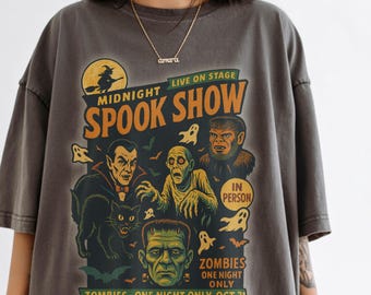 May include: Dark gray t-shirt featuring a vintage-style "Midnight Spook Show" design. The graphic includes illustrations of classic monsters like Dracula, Frankenstein's monster, a werewolf, and zombies, with the text "Zombies One Night Only Oct 31".
