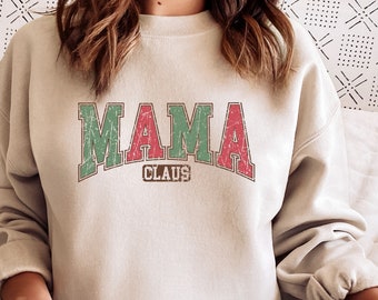 Op de afbeelding: Een licht beige sweatshirt met de tekst "MAMA CLAUS" in rode en groene letters. De letters zijn in een vintage lettertype.