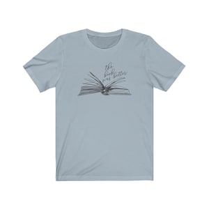 May include: Light blue t-shirt with a black and white illustration of an open book. The text "the book was better" is written above the book.