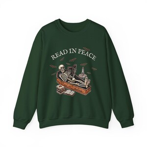 May include: A dark green sweatshirt with a skeleton reading a book in a coffin. The text "READ IN PEACE" is printed above the skeleton.