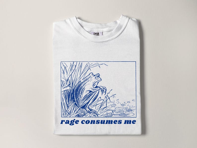 May include: White t-shirt with a blue line drawing of a frog in a pond with the text "rage consumes me" printed in blue.