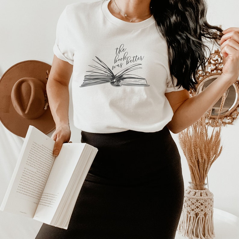 May include: White t-shirt with a black and white illustration of an open book and the text "the book was better".