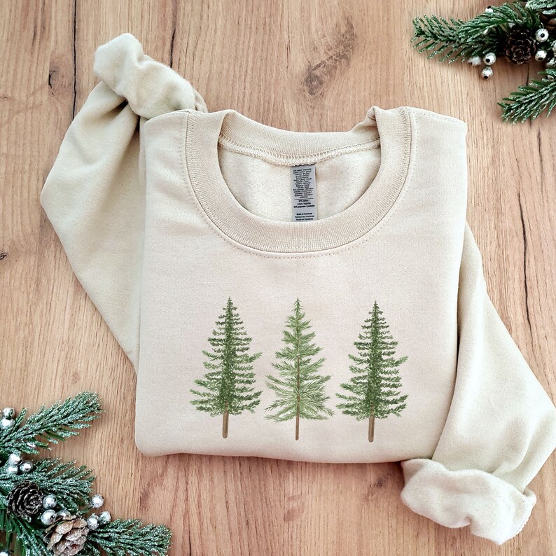 May include: A beige sweatshirt with a graphic of three green pine trees on the front.