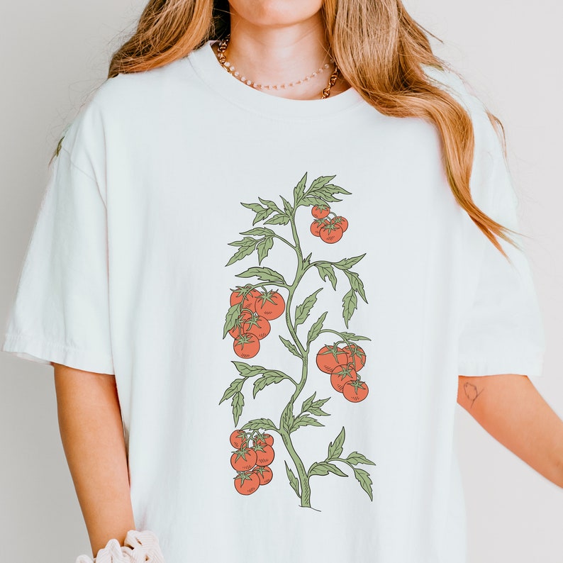 May include: White t-shirt with a graphic of a tomato plant with red tomatoes and green leaves.
