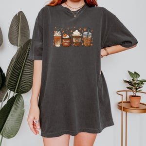 May include: A black oversized t-shirt with a graphic of four fall-themed coffee drinks. The drinks are labeled "Pumpkin Spice" and have fall leaves around them.