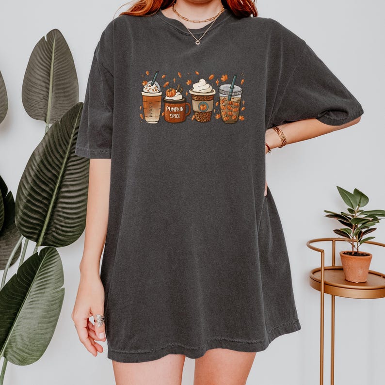 May include: A black oversized t-shirt with a graphic of four fall-themed coffee drinks. The drinks are labeled "Pumpkin Spice" and have fall leaves around them.