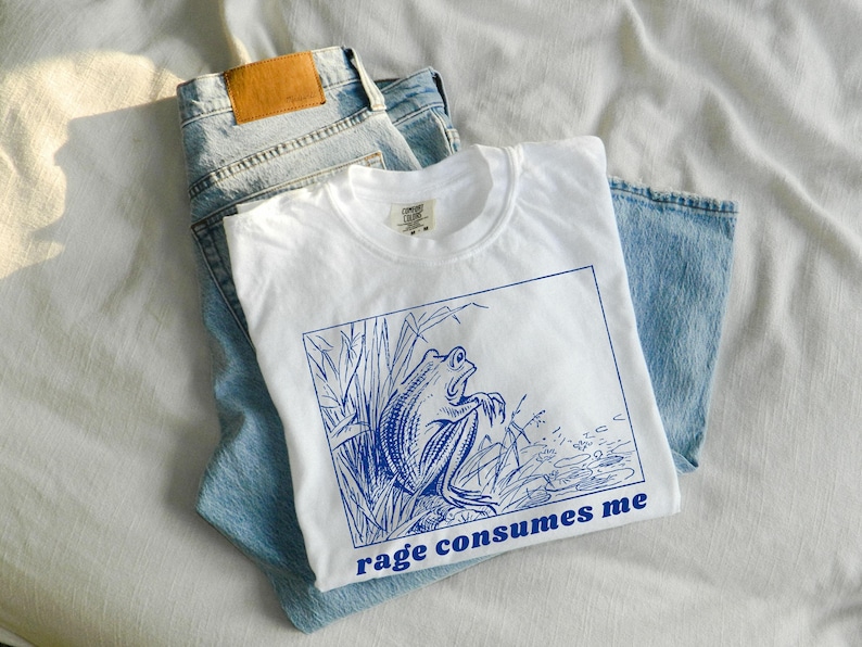 May include: White t-shirt with a blue illustration of a frog in a swamp with the text "rage consumes me".