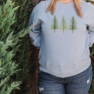 May include: A light blue sweatshirt with a design of three green pine trees on the front.
