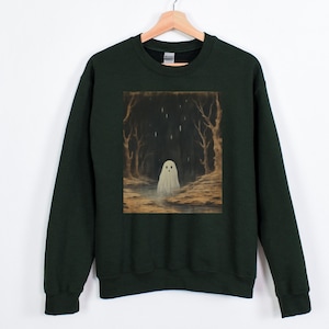 Puede incluir: Una sudadera verde oscuro con un fantasma blanco en una escena de bosque impresa en la parte delantera. El fantasma tiene una cara blanca con dos ojos negros y una peque&ntilde;a boca.