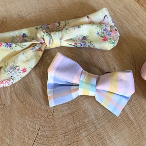 Puede incluir: Una diadema floral amarilla y una pajarita de cuadros pastel sobre una superficie de madera. También hay dos huevos de Pascua moteados sobre la superficie.