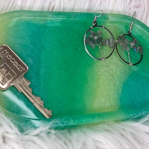 May include: A green and yellow oval-shaped resin tray with a silver key and a pair of silver earrings with blue and gray stones.