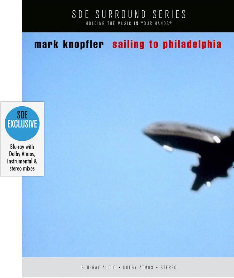 May include: Blu-ray disc cover for "Sailing to Philadelphia" by Mark Knopfler. The cover features a blurred image of an airplane against a light blue sky. Text includes "SDE SURROUND SERIES" and "SDE EXCLUSIVE".