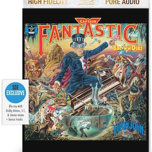 May include: Blu-ray disc of "Captain Fantastic and the Brown Dirt Cowboy" by Elton John. The cover art shows a whimsical illustration of a man in a blue suit and top hat, playing a piano. The disc is labelled "SDE Exclusive" with bonus tracks.
