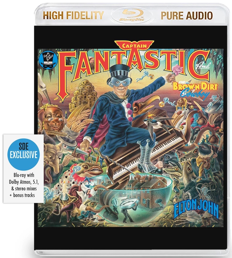 May include: Blu-ray disc of "Captain Fantastic and the Brown Dirt Cowboy" by Elton John. The cover art shows a whimsical illustration of a man in a blue suit and top hat, playing a piano. The disc is labelled "SDE Exclusive" with bonus tracks.