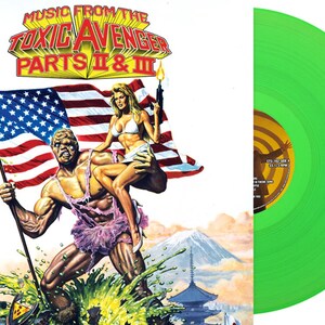May include: A green vinyl record with the title "Music From The Toxic Avenger Parts II & III" in white text. The cover art features a muscular green man holding an American flag and a woman in a bikini.