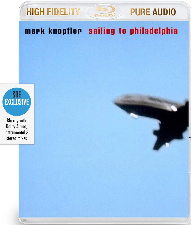 May include: Blu-ray disc case for Mark Knopfler's album "Sailing to Philadelphia." The cover features the album title and artist name in black and red text against a light blue sky. A blurred image of an airplane is in the background.