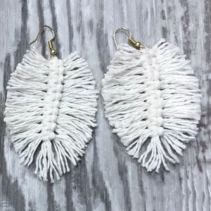 May include: A pair of white feather earrings with gold hooks. The earrings are made of macrame and have a fringed design.