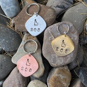 May include: Three keychains with a silver, copper, and brass finish. Each keychain features a cutout of the state of Idaho and the number 208.