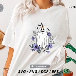 May include: White t-shirt featuring a Halloween-themed design. The graphic includes a smiling ghost with a pumpkin head, surrounded by purple flowers and a black bat. The word "Cutting" is printed on the shirt.