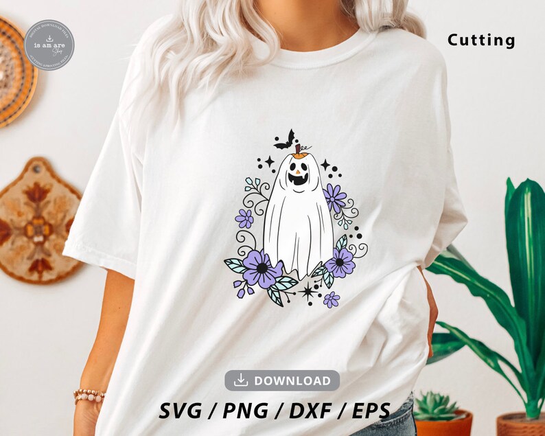 May include: White t-shirt featuring a Halloween-themed design. The graphic includes a smiling ghost with a pumpkin head, surrounded by purple flowers and a black bat. The word "Cutting" is printed on the shirt.