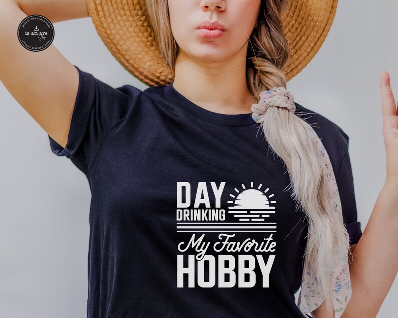Puede incluir: Camiseta negra con texto blanco que dice "Day Drinking My Favorite Hobby" con un gr&aacute;fico de puesta de sol.