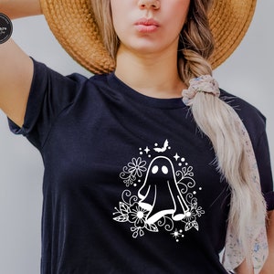May include: A black t-shirt with a white graphic of a ghost surrounded by flowers and a bat. The ghost has two eyes and a small mouth.