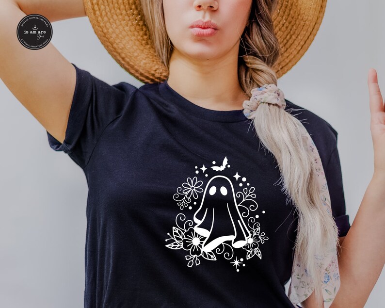 May include: A black t-shirt with a white graphic of a ghost surrounded by flowers and a bat. The ghost has two eyes and a small mouth.