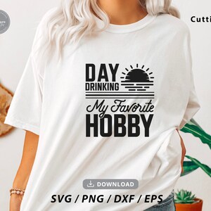 Puede incluir: Camiseta blanca con texto negro que dice "Day Drinking My Favorite Hobby" con un gr&aacute;fico de sol y olas.