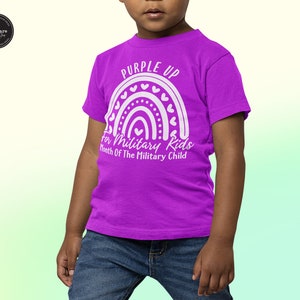 May include: A purple t-shirt with a white rainbow design and the text "Purple Up for Military Kids Month of the Military Child".