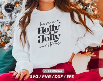 May include: White sweatshirt with the text "have a Holly Jolly christmas" in black lettering. The sweatshirt is being worn by a person sitting on a red and white plaid blanket.