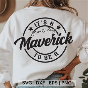 Può includere: Felpa bianca con un design circolare nero che recita "It's a great day Maverick to be a" con accenti a stella. La parte inferiore dell'immagine mostra il testo "SVG | DXF | EPS | PNG".