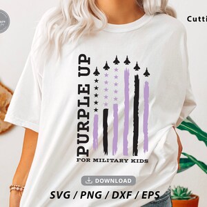 May include: White t-shirt with a purple up for military kids design. The design features a purple and black American flag with stars and aeroplanes.
