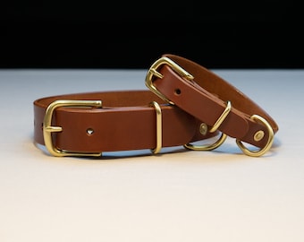 May include: Two brown leather dog collars with brass fittings. The collars are different sizes, featuring a buckle and a D-ring for lead attachment. The leather has a warm tone, and the brass hardware adds a touch of elegance. These collars are designed for pet accessories.