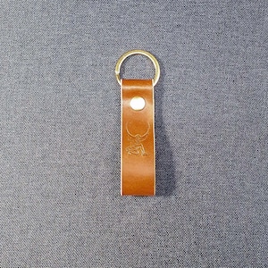 May include: A brown leather keychain with a gold metal ring. The keychain has a small, embossed design of a bull.
