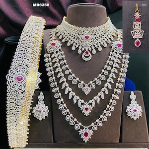 May include: A bridal jewelry set with a diamond necklace, earrings, and a waist belt. The set features a large, ornate design with red gemstones. The set is labeled "MB6250".