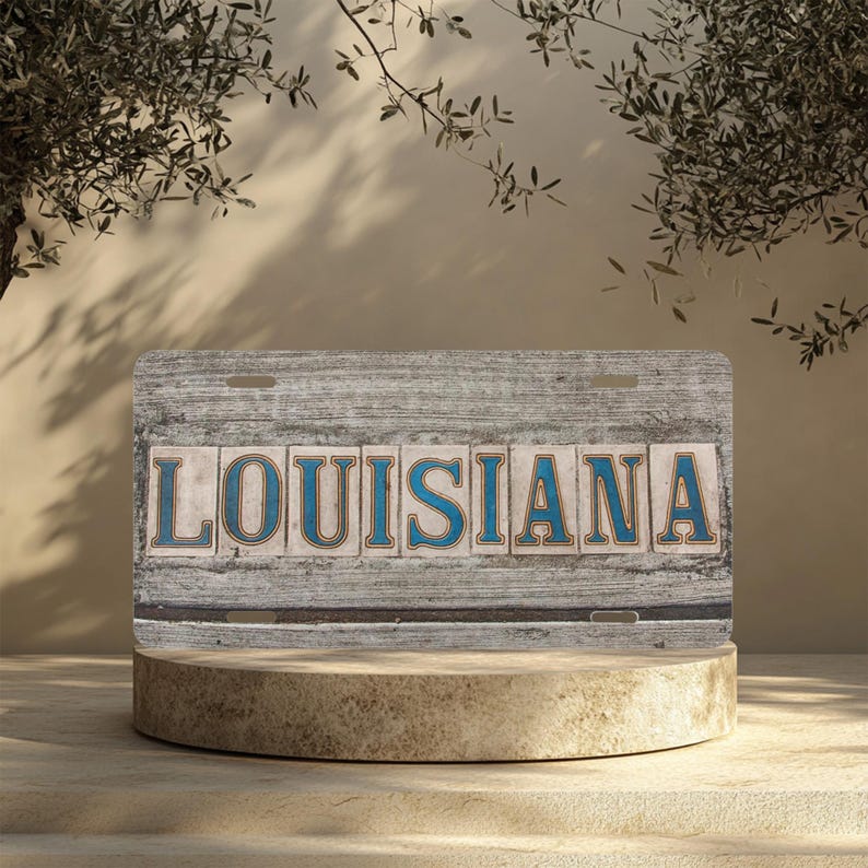 May include: A vintage-style metal sign with the word "LOUISIANA" in blue letters on a white background. The sign is weathered and has a rustic look.