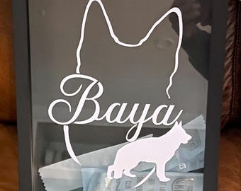 May include: A black framed shadow box featuring a white silhouette of a German Shepherd dog and the name "Baya" in cursive script. The box contains a selection of dog treats.