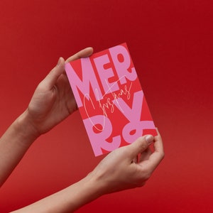Könnte beinhalten: Eine rosa und rote Weihnachtskarte mit dem Text "Merry Christmas" in einer fetten, modernen Schrift.