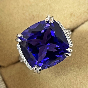 May include: A silver ring with a large, cushion-cut, deep blue sapphire gemstone surrounded by a halo of smaller diamonds.