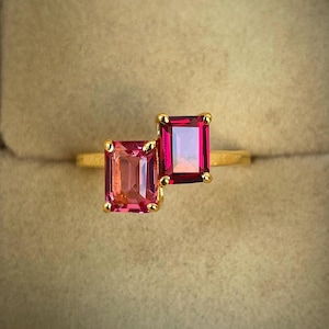 May include: Gold ring with two pink and red emerald-cut gemstones.