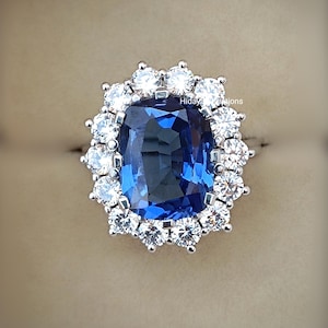 May include: A large, cushion-cut sapphire ring surrounded by a halo of smaller diamonds. The ring is set in a white metal band.