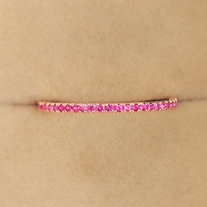 Peut inclure: Une délicate bague éternelle avec une rangée continue de petites pierres précieuses roses serties dans une bande d'or.