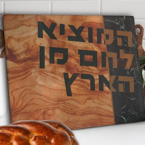 Shabbat challah cutting board made of tempered glass is propped against a wall. It has a printed image of wood and green marble with bold Hebrew blessing Hamotzi Lechem Min Haaretz for bread.
Shabbat cutting board for challah jewish wedding gift