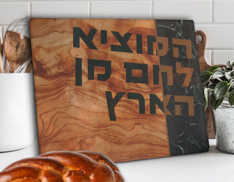 Shabbat challah cutting board made of tempered glass is propped against a wall. It has a printed image of wood and green marble with bold Hebrew blessing Hamotzi Lechem Min Haaretz for bread.
Shabbat cutting board for challah jewish wedding gift