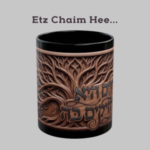 May include: Black and brown ceramic mug with a detailed tree of life design. The mug features Hebrew text and the words "Etz Chaim Hee..." at the top. The tree design is carved into the mug's surface.