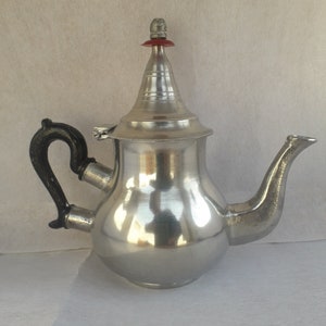 May include: A silver teapot with a black handle and a red and silver lid. The teapot has a round body and a spout on the right side.