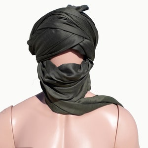 May include: A dark green headscarf is worn on a mannequin's head. The scarf is folded and tied in a way that covers the mannequin's face.