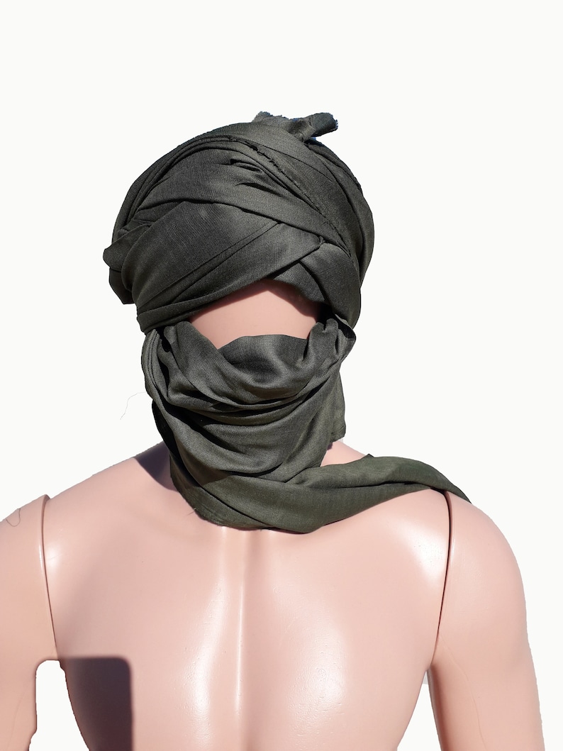 May include: A dark green headscarf is worn on a mannequin's head. The scarf is folded and tied in a way that covers the mannequin's face.