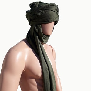 May include: A green fabric head covering, worn as a turban, with the ends draped down the front of the neck.