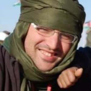 May include: A man wearing a green scarf and a black jacket with a red lanyard. He is smiling and looking at the camera.